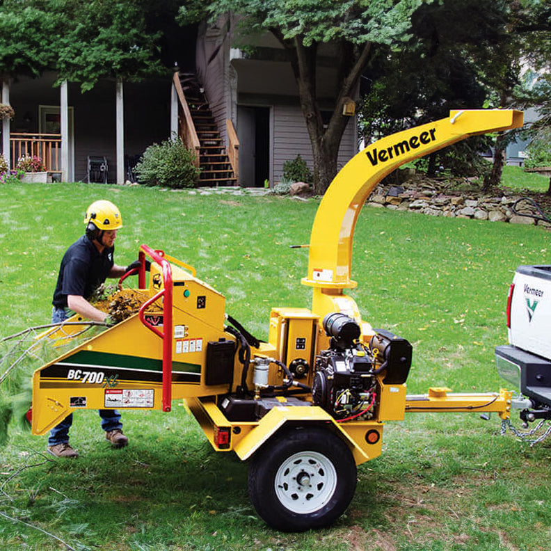 A 6-inch wood chipper in action with a man pushing branches through the hopper on-site.